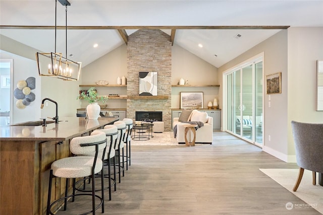 kitchen featuring vaulted ceiling with beams, light wood-type flooring, a breakfast bar area, hanging light fixtures, and a stone fireplace