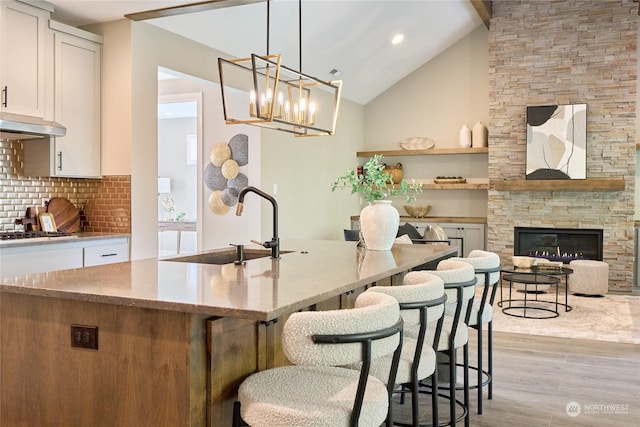 kitchen featuring pendant lighting, light hardwood / wood-style floors, decorative backsplash, white cabinets, and a fireplace