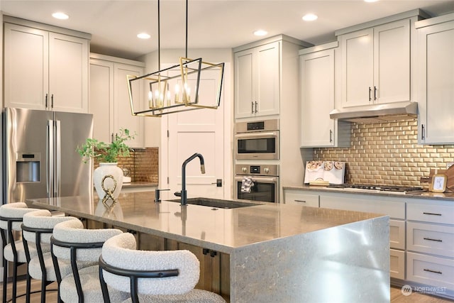 kitchen with stainless steel appliances, sink, decorative light fixtures, decorative backsplash, and a center island with sink