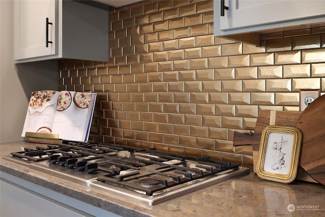 room details featuring stainless steel gas cooktop, backsplash, and white cabinetry