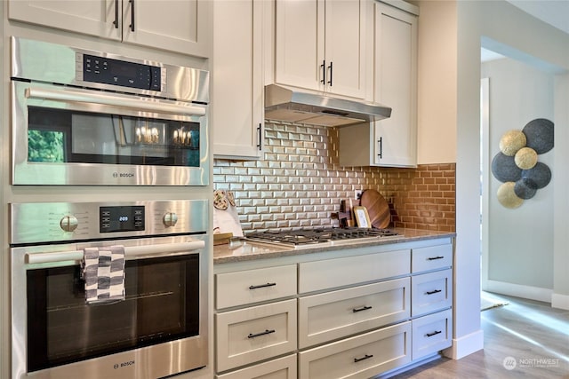 kitchen with appliances with stainless steel finishes, decorative backsplash, white cabinetry, and light stone countertops