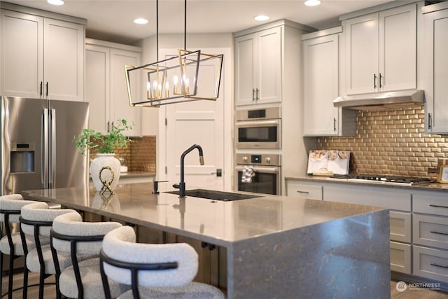 kitchen featuring sink, a kitchen breakfast bar, an island with sink, backsplash, and appliances with stainless steel finishes