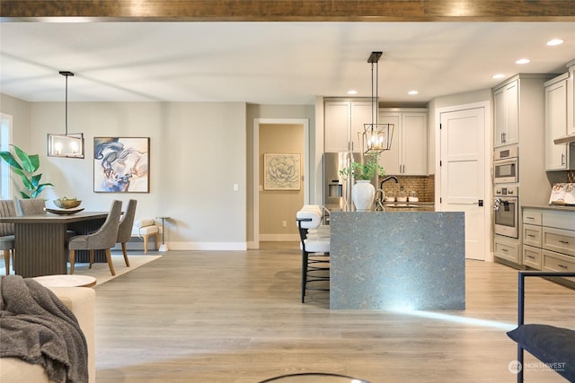 kitchen with light wood-type flooring, backsplash, hanging light fixtures, and appliances with stainless steel finishes