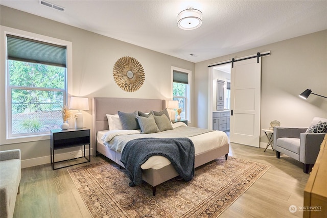 bedroom featuring ensuite bath, a barn door, and light hardwood / wood-style flooring