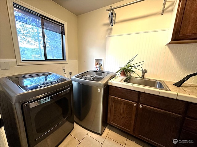 clothes washing area featuring cabinets, light tile patterned flooring, washer and clothes dryer, and sink