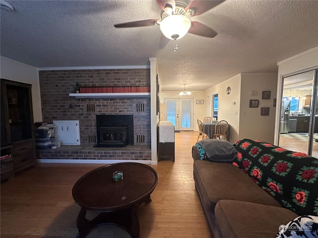 living room featuring a textured ceiling, a wood stove, ornamental molding, ceiling fan with notable chandelier, and wood-type flooring