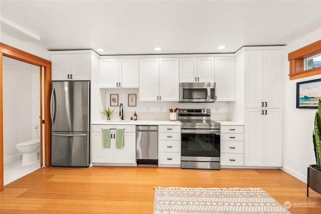 kitchen with stainless steel appliances, white cabinets, sink, and light hardwood / wood-style floors