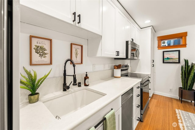 kitchen with stainless steel appliances, white cabinetry, sink, and light wood-type flooring