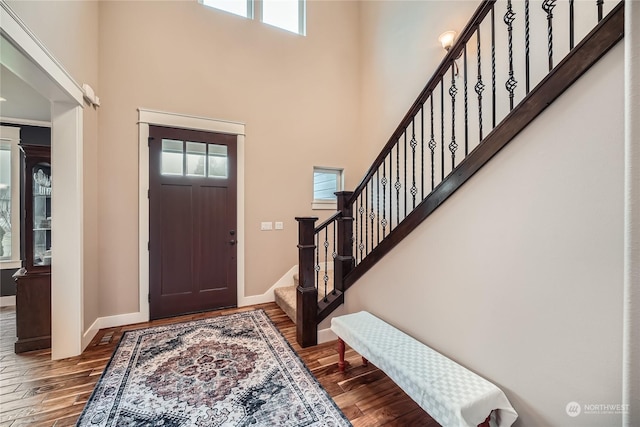 foyer entrance with stairway, a high ceiling, baseboards, and wood finished floors