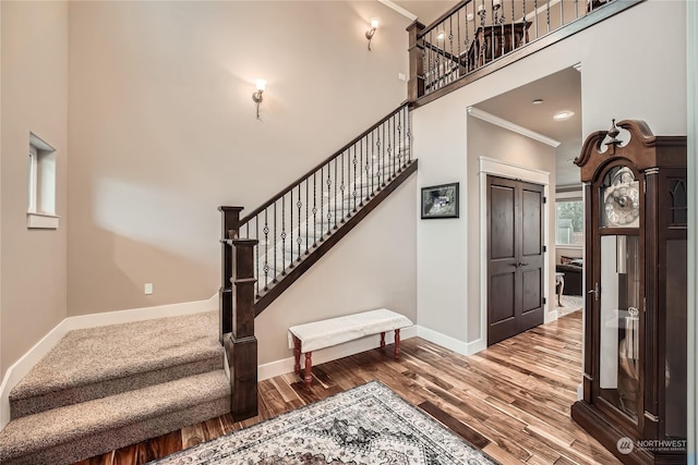 stairs with hardwood / wood-style floors, ornamental molding, and a high ceiling