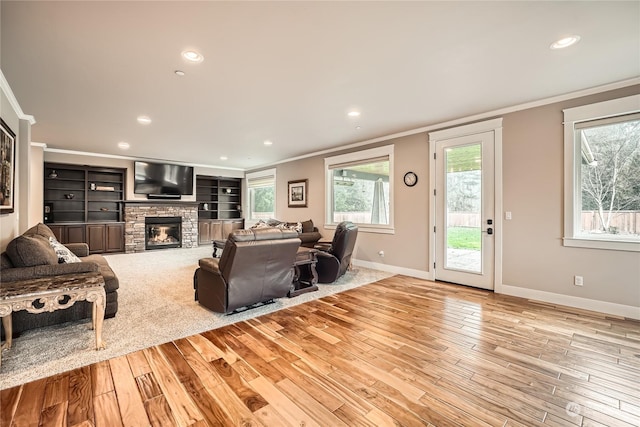 living room with light wood finished floors, a stone fireplace, baseboards, and crown molding