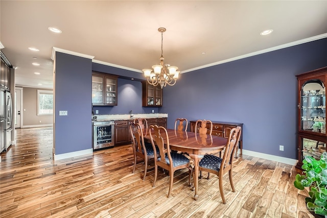 dining space featuring beverage cooler, baseboards, light wood-style flooring, ornamental molding, and indoor wet bar