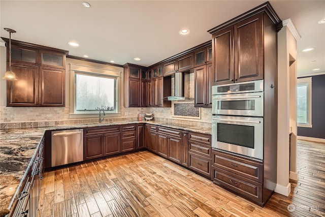 kitchen featuring dark brown cabinetry, decorative backsplash, stainless steel appliances, light wood-type flooring, and wall chimney range hood