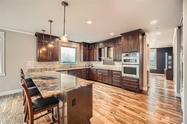 kitchen featuring a breakfast bar area, tasteful backsplash, dark brown cabinetry, a peninsula, and wall chimney exhaust hood