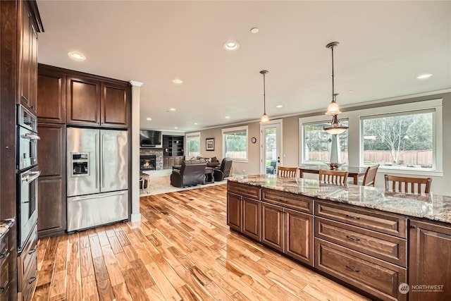 kitchen featuring a fireplace, stainless steel appliances, hanging light fixtures, dark brown cabinetry, and light wood-type flooring