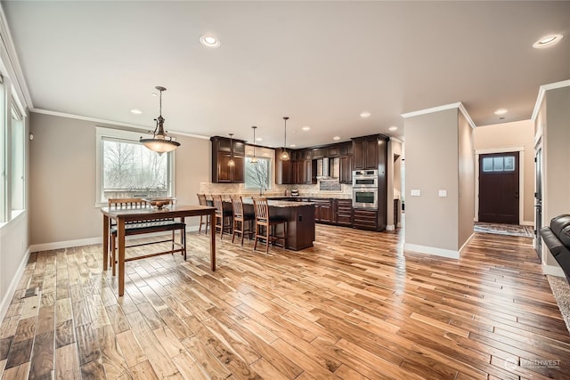 interior space with a kitchen island, decorative light fixtures, a breakfast bar area, dark brown cabinetry, and stainless steel double oven