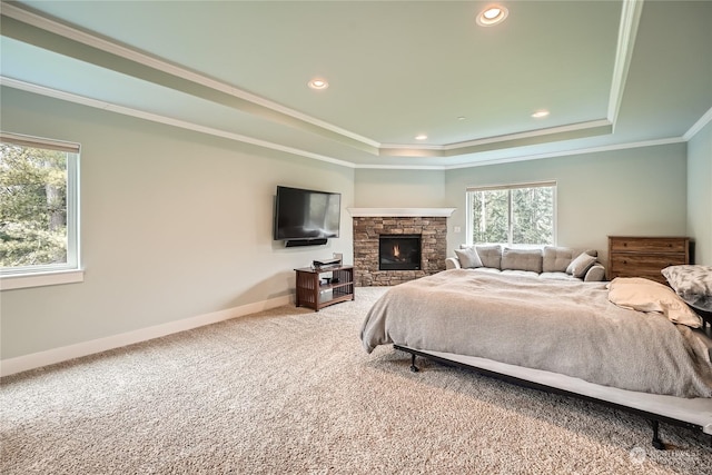 carpeted bedroom with a raised ceiling, ornamental molding, and a stone fireplace