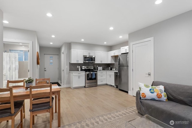 kitchen with stainless steel appliances, white cabinetry, backsplash, and light hardwood / wood-style flooring