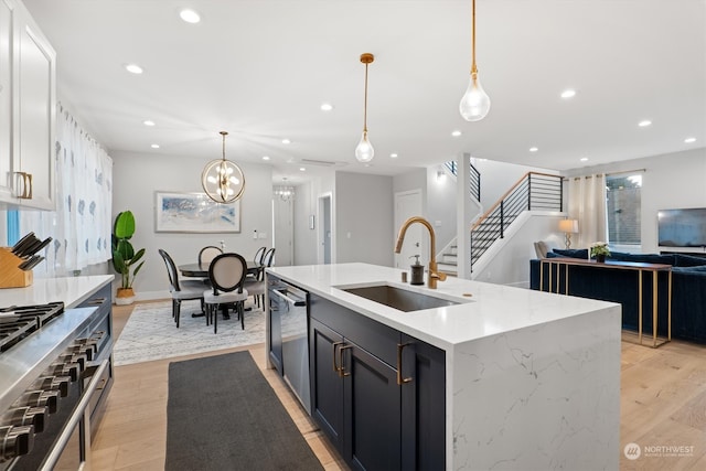 kitchen featuring decorative light fixtures, a kitchen island with sink, sink, and light hardwood / wood-style flooring