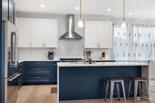 kitchen with white cabinetry, high end refrigerator, decorative light fixtures, and wall chimney range hood