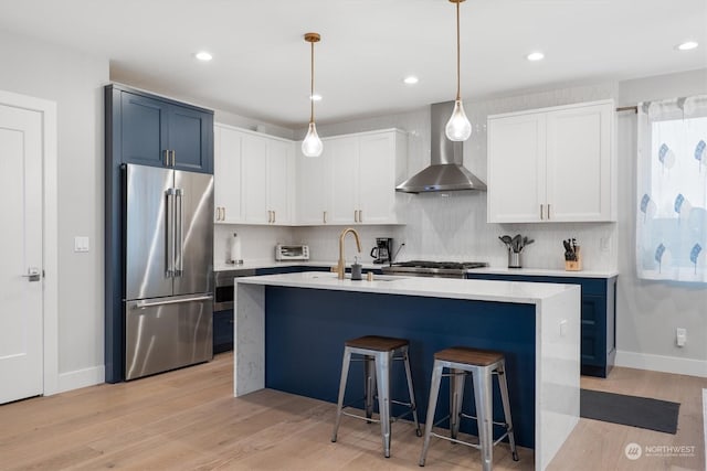 kitchen featuring decorative light fixtures, sink, white cabinets, high end fridge, and wall chimney range hood