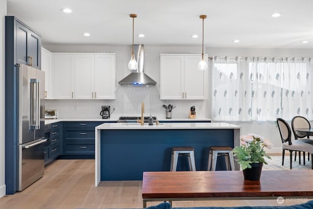 kitchen featuring wall chimney range hood, hanging light fixtures, high end refrigerator, and white cabinets