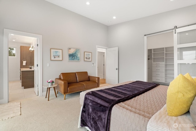 carpeted bedroom with a walk in closet, a barn door, ensuite bath, and a closet