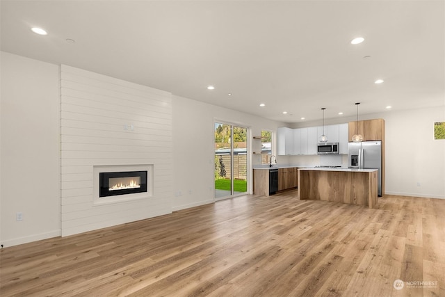 kitchen featuring a large fireplace, stainless steel appliances, a center island, sink, and decorative light fixtures