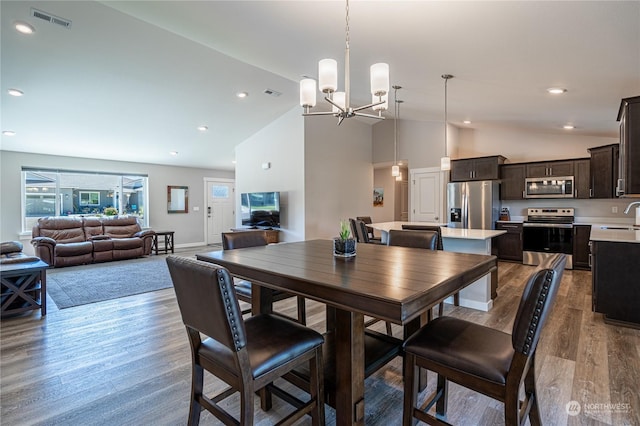 dining area with a notable chandelier, hardwood / wood-style floors, lofted ceiling, and sink