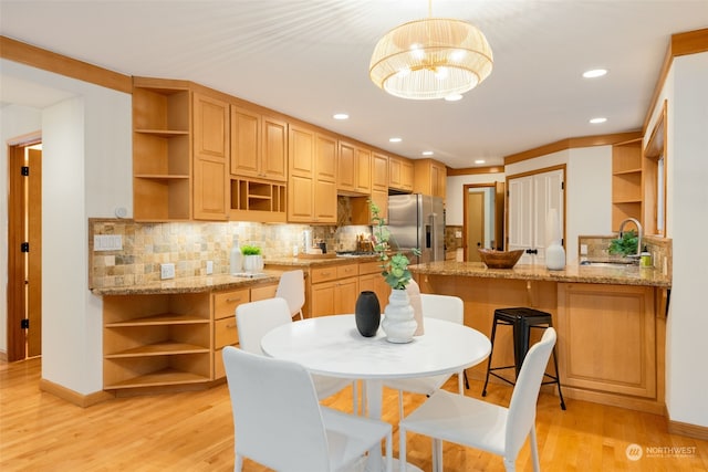 kitchen with sink, hanging light fixtures, light stone counters, kitchen peninsula, and high end fridge