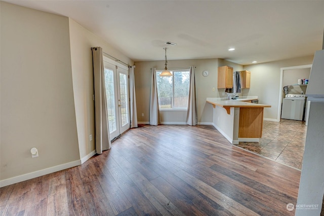 kitchen featuring washer / clothes dryer, french doors, light hardwood / wood-style flooring, kitchen peninsula, and a breakfast bar