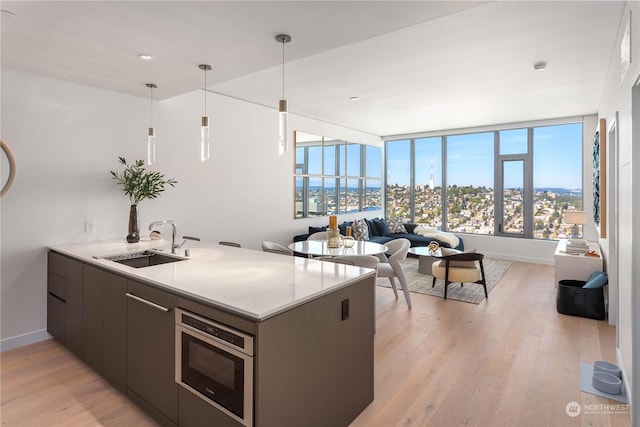 kitchen featuring kitchen peninsula, stainless steel microwave, sink, light hardwood / wood-style flooring, and decorative light fixtures