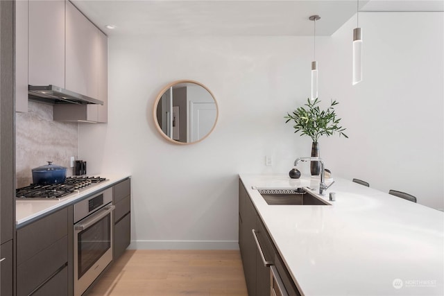 kitchen featuring gray cabinets, appliances with stainless steel finishes, light hardwood / wood-style floors, pendant lighting, and sink