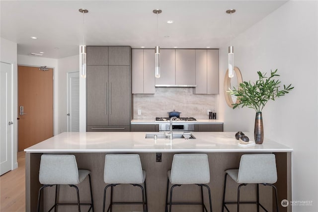 kitchen with decorative light fixtures, a kitchen bar, gray cabinets, backsplash, and sink