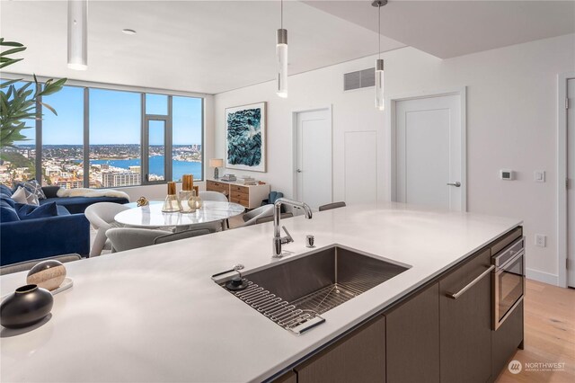 kitchen featuring sink, oven, decorative light fixtures, a water view, and light hardwood / wood-style floors