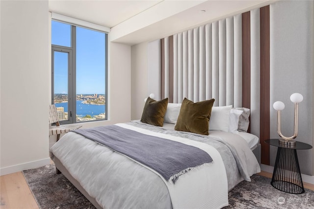 bedroom featuring a water view, expansive windows, and wood-type flooring