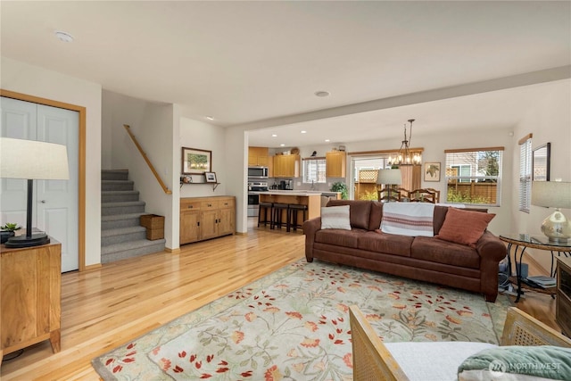 living room featuring light wood finished floors, a notable chandelier, recessed lighting, and stairs