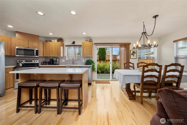 kitchen featuring light wood-style flooring, a kitchen island, appliances with stainless steel finishes, light countertops, and decorative backsplash