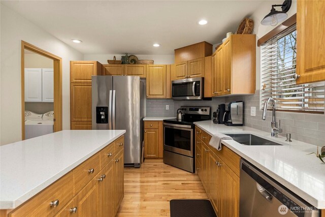 kitchen with light wood finished floors, a sink, light countertops, appliances with stainless steel finishes, and washer and dryer