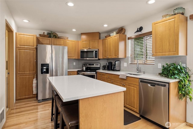 kitchen featuring light wood-type flooring, a sink, a center island, appliances with stainless steel finishes, and light countertops