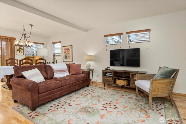 living area featuring beam ceiling, light wood finished floors, and a chandelier