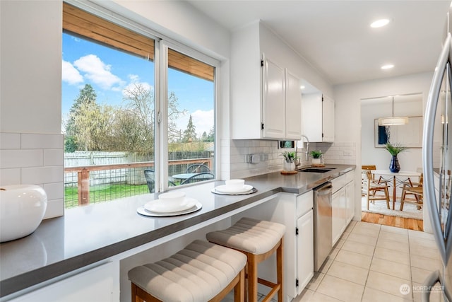 kitchen featuring appliances with stainless steel finishes, backsplash, white cabinets, a breakfast bar, and sink