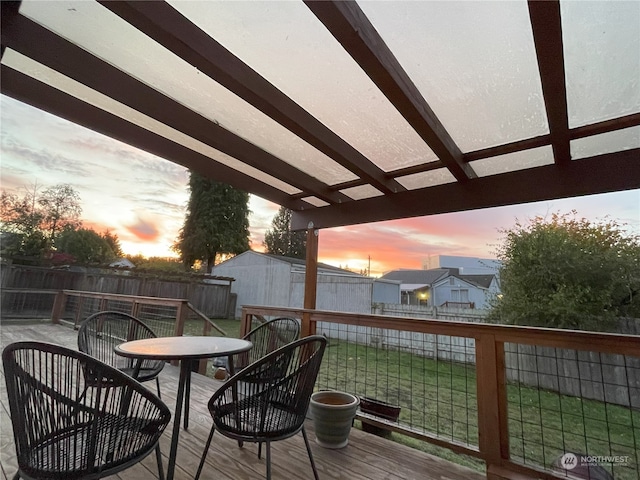 deck at dusk featuring a yard and a storage unit