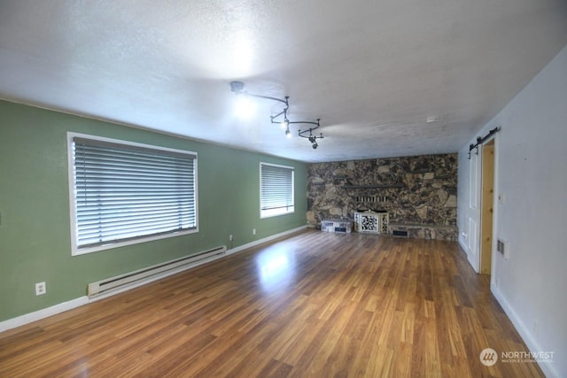 unfurnished living room with baseboard heating, a textured ceiling, a barn door, and wood-type flooring