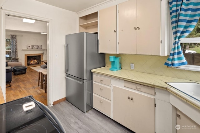 kitchen featuring white cabinetry, light hardwood / wood-style floors, tasteful backsplash, stainless steel refrigerator, and electric range