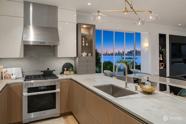 kitchen featuring wall chimney exhaust hood, sink, backsplash, stainless steel stove, and light stone counters