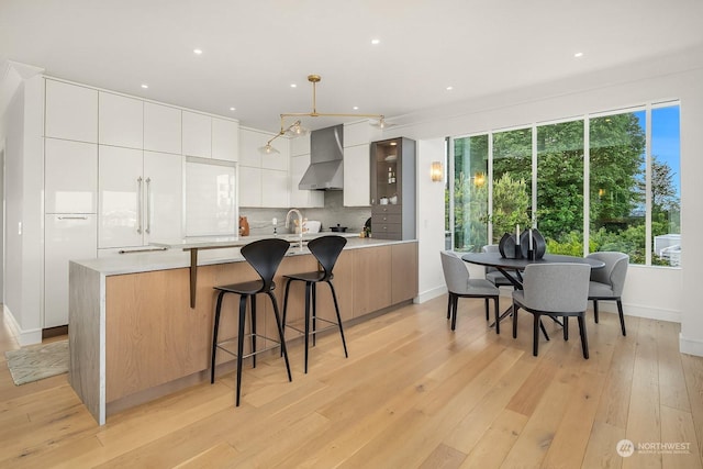 kitchen featuring decorative backsplash, white cabinetry, wall chimney range hood, and light wood-type flooring