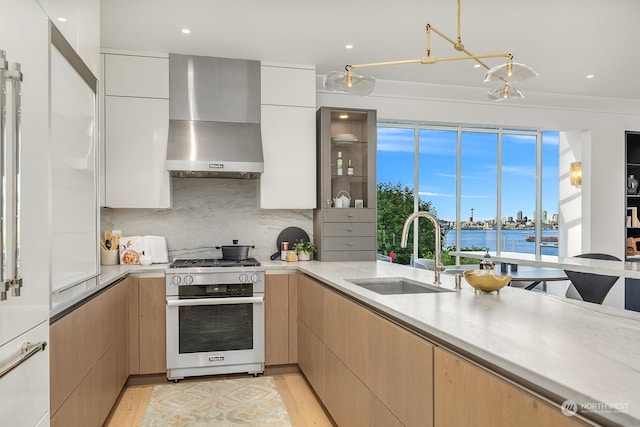 kitchen featuring stainless steel range, wall chimney range hood, light brown cabinets, sink, and a water view