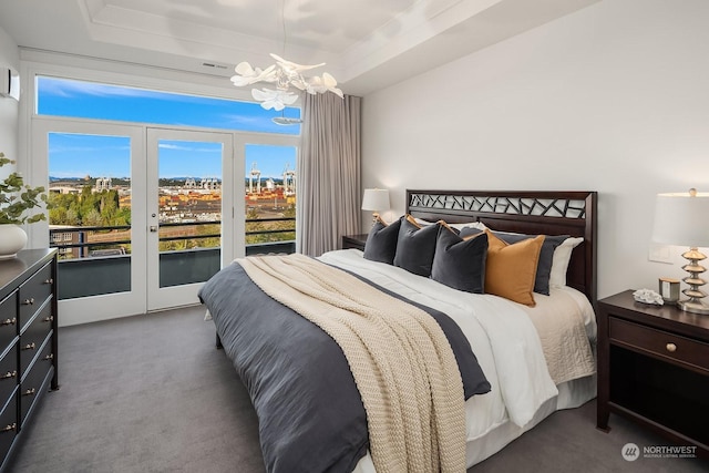 carpeted bedroom with access to exterior, a notable chandelier, and a tray ceiling