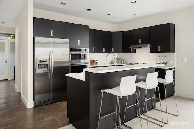 kitchen featuring a kitchen breakfast bar, backsplash, appliances with stainless steel finishes, and a center island with sink